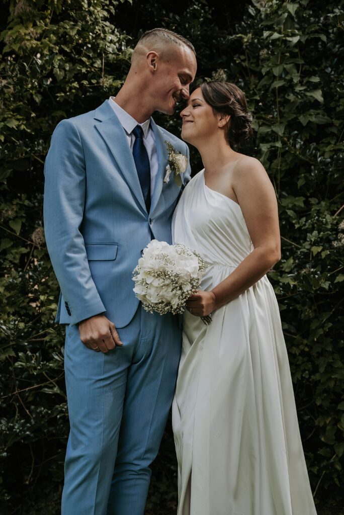 Hochzeitsfotograf Krefeld - Braut und Bräutigam teilen einen romantischen Kuss vor einer idyllischen Hochzeitskulisse mit Grün im Hintergrund.