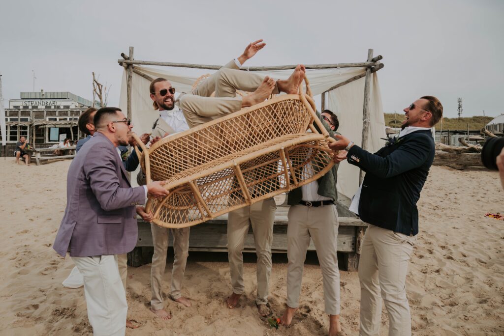 Freunde werfen den Bräutigam hoch, ausgelassene Stimmung nach der Strandtrauung in Castricum