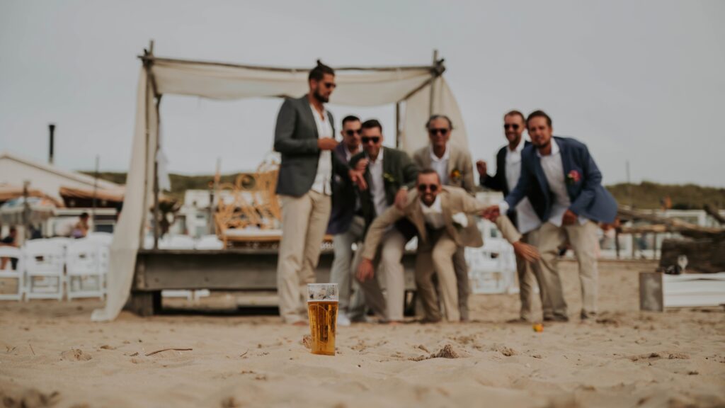 Bräutigam und Freunde rennen am Strand zum Bier, lachend und ausgelassen
