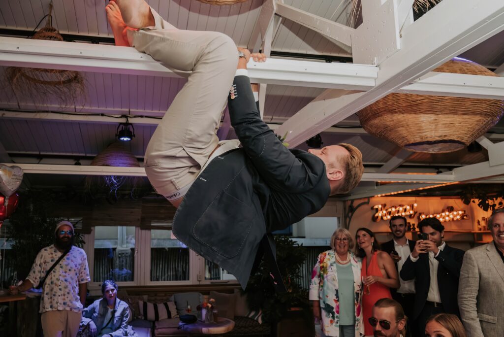 Ausgelassene Hochzeitsparty – Gast hängt an einem Balken und feiert auf der Tanzfläche