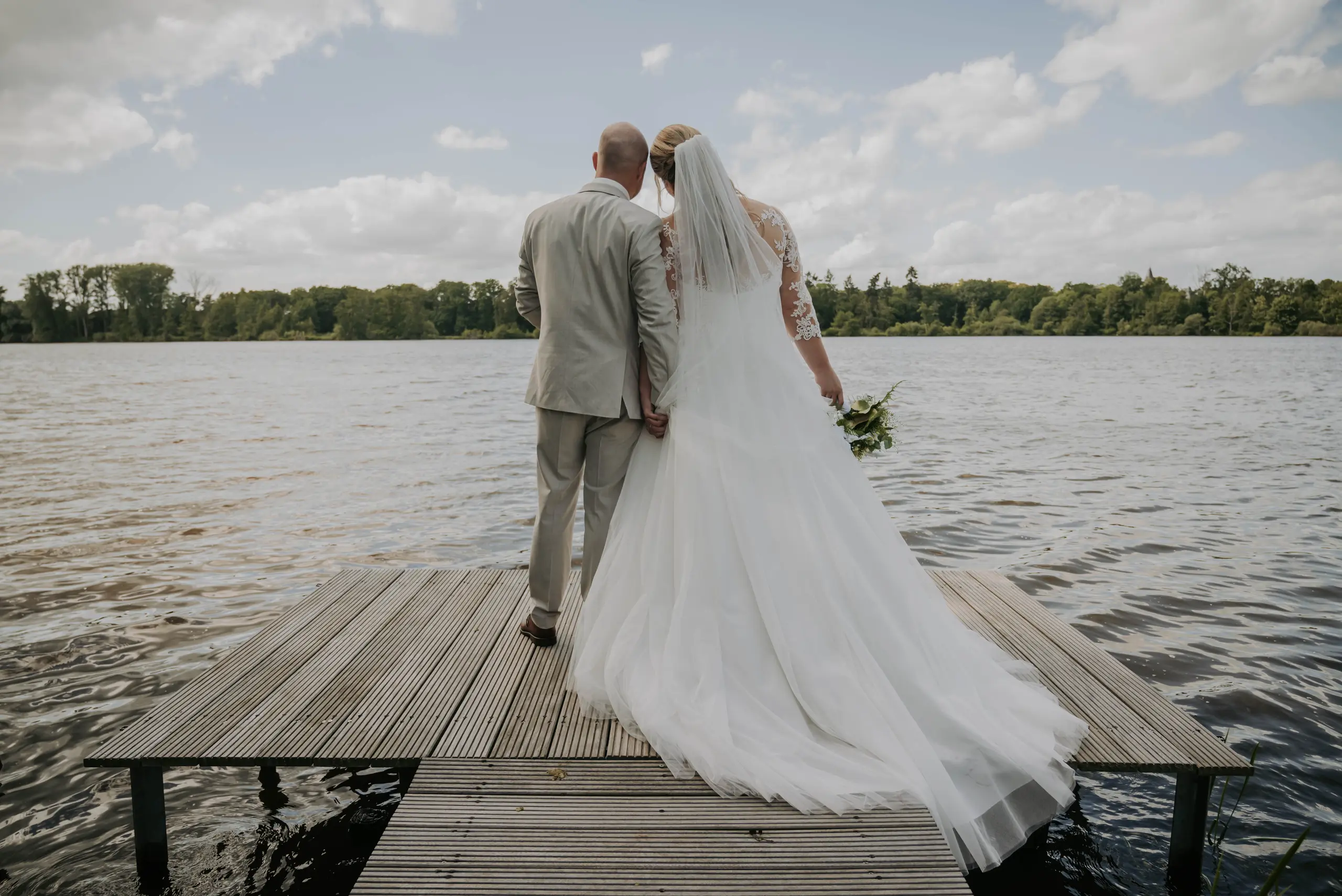 Marina und Dennis stehen von hinten auf dem Steg und schauen auf den See