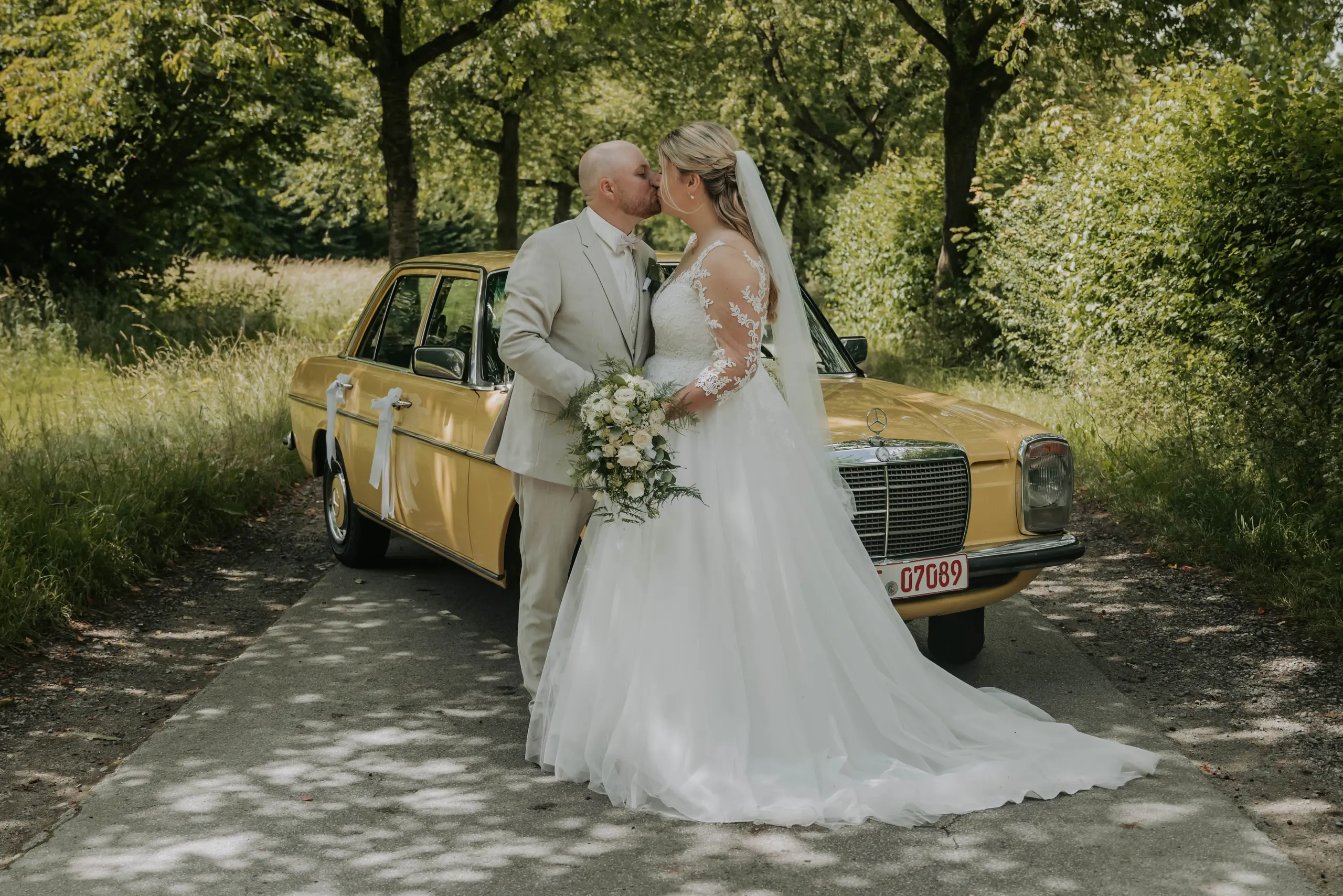 Marina und Dennis küssen sich vor ihrem gelben Mercedes-Oldtimer