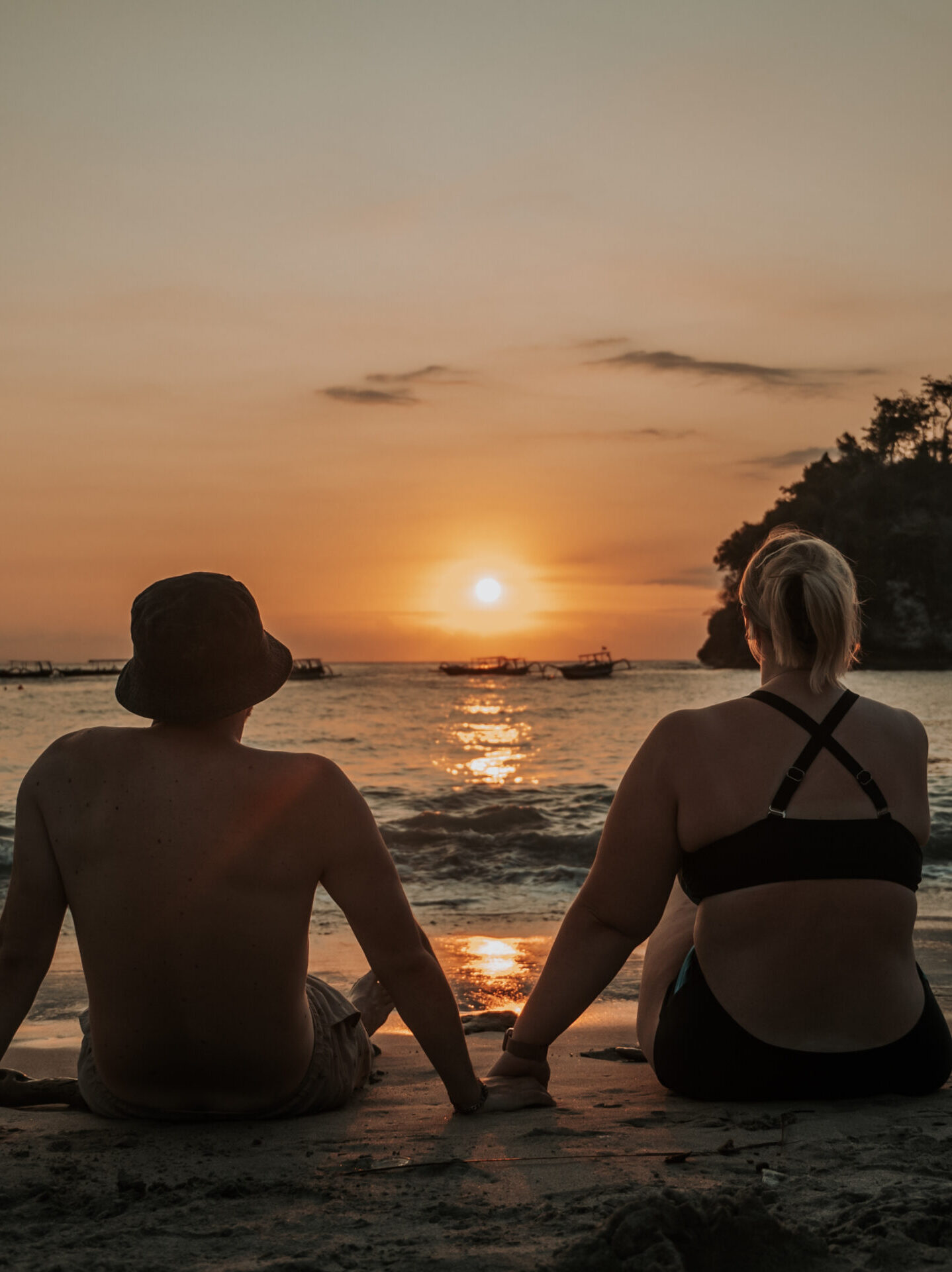 Nathalie und Christian sitzen gemeinsam am Strand bei Sonnenuntergang