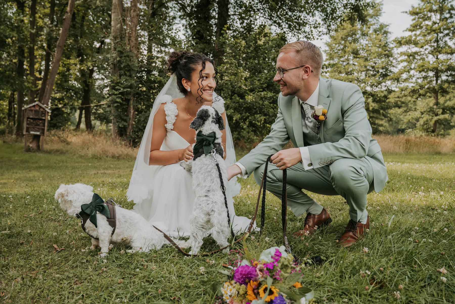 Brautpaar sitzt mit seinem Hund im Grünen.